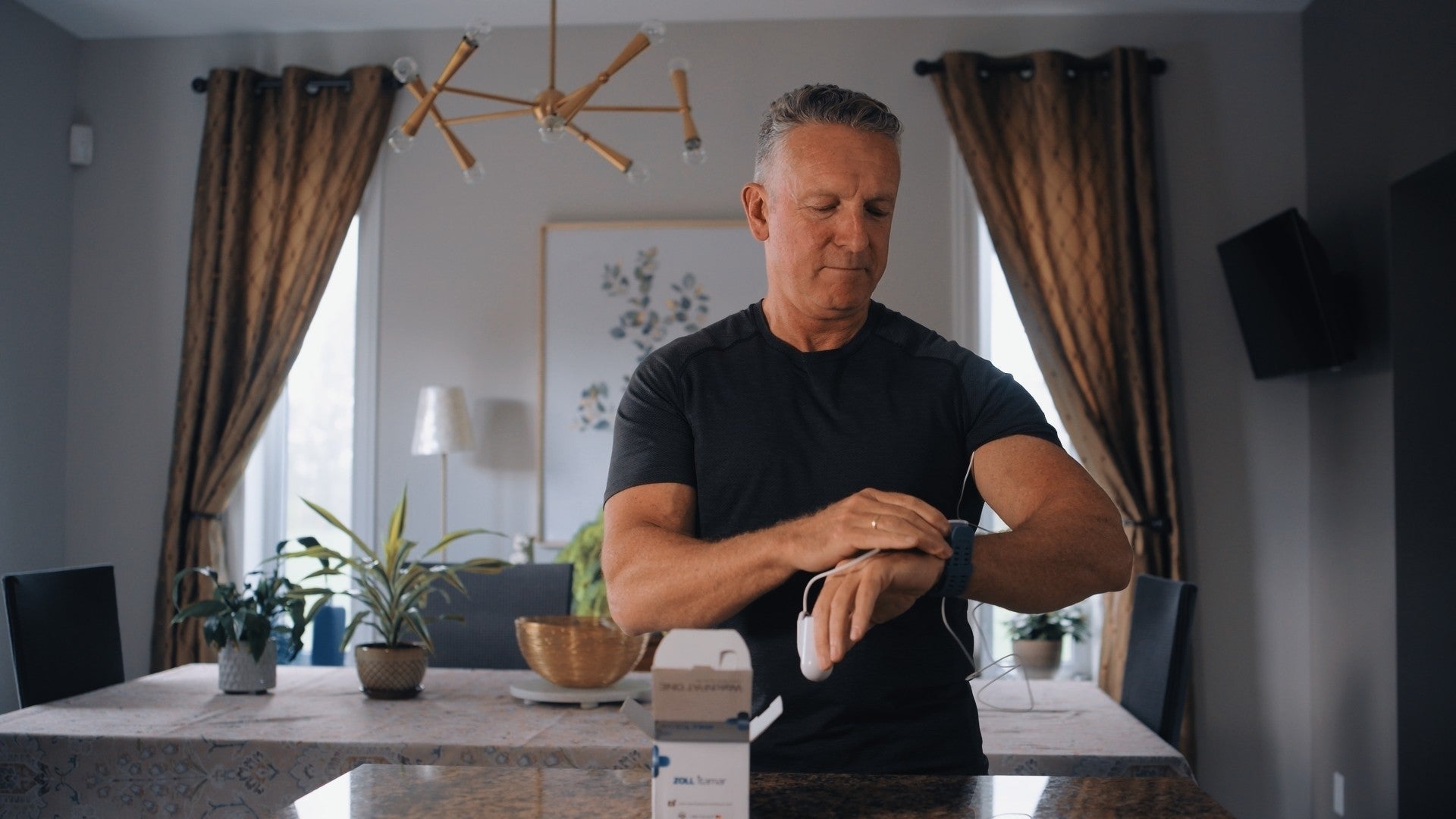 A man puts on the WatchPAT ONE sensor on his wrist at home, the device box open on the counter